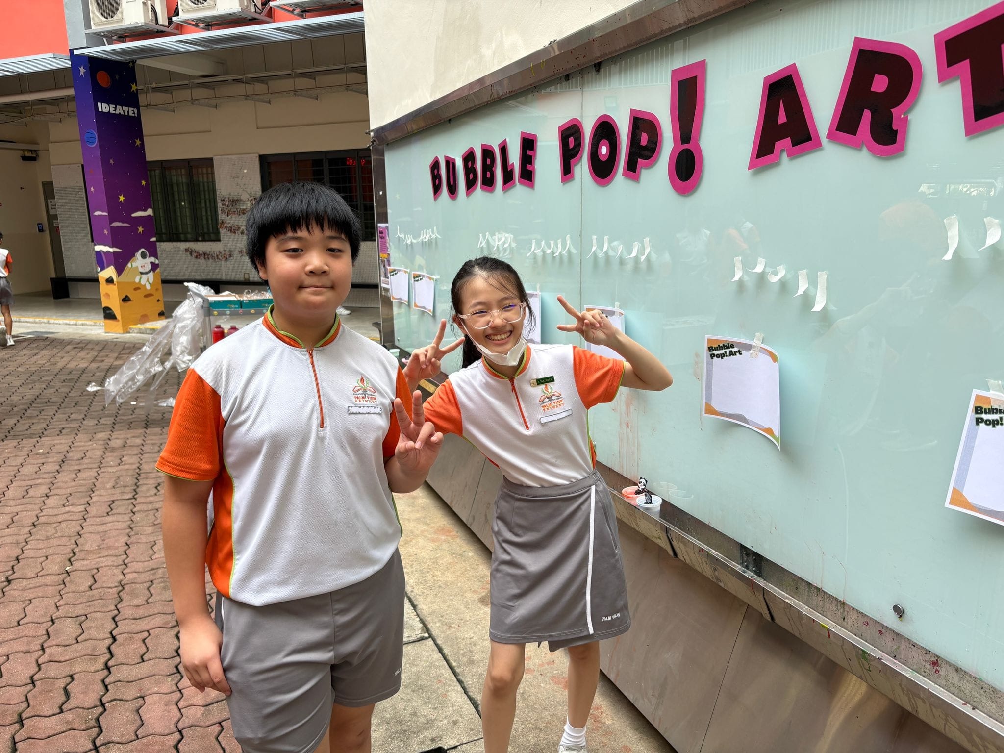 Two students smiling and posing in front of the Bubble Pop Art recess activity wall